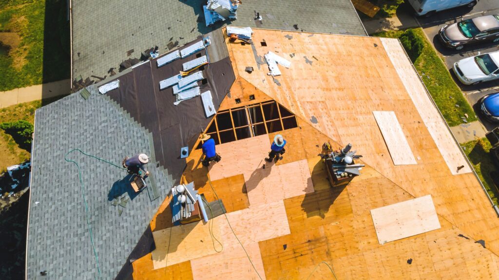 Aerial view of workers repairing a Huntsville home roof with exposed plywood decking