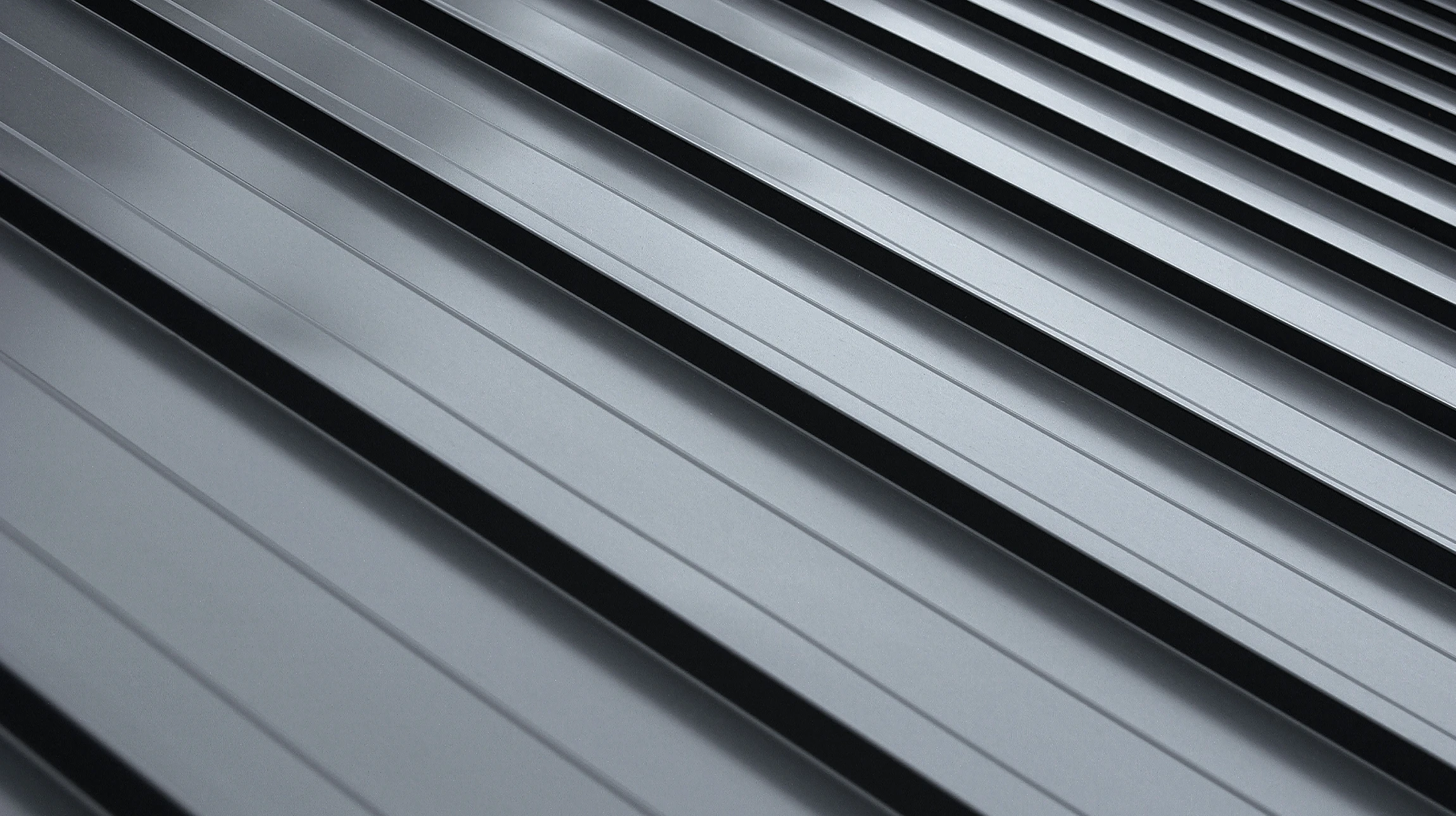 Close-up view of a gray metal roof with evenly spaced parallel ridges running diagonally across the image, creating a modern and industrial appearance.