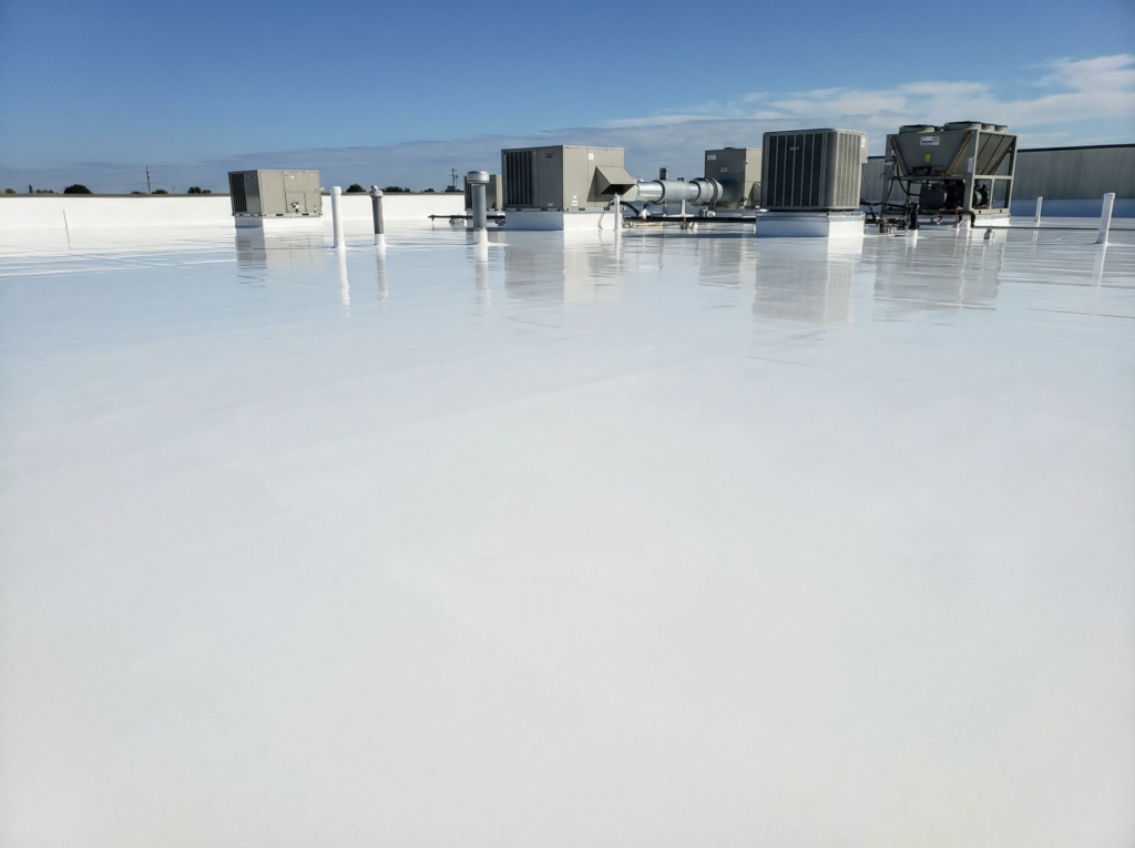 A flat, white commercial building rooftop with HVAC units under a clear blue sky, with a smooth reflective coated surface.