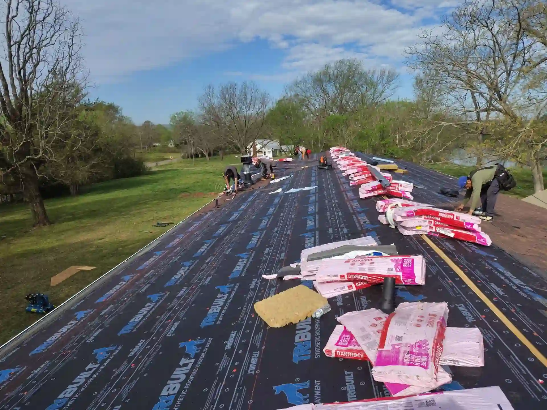 Roofers installing shingles over fresh underlayment with bundles staged across the roof deck