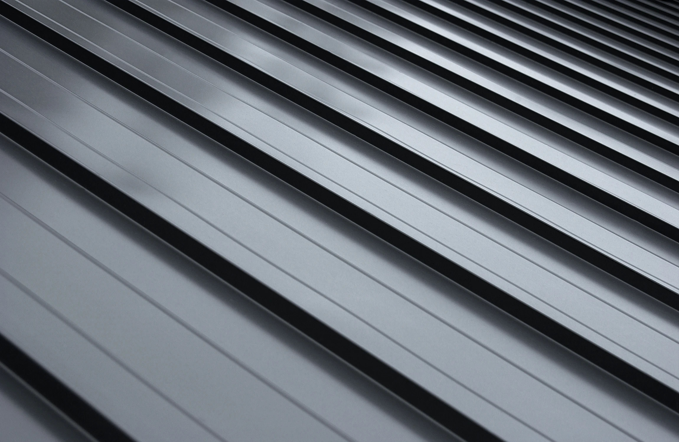 Close-up view of a modern metal roof with parallel, raised seams running diagonally, creating a sleek and industrial appearance. The surface is smooth and reflective, emphasizing the clean lines and geometric pattern.