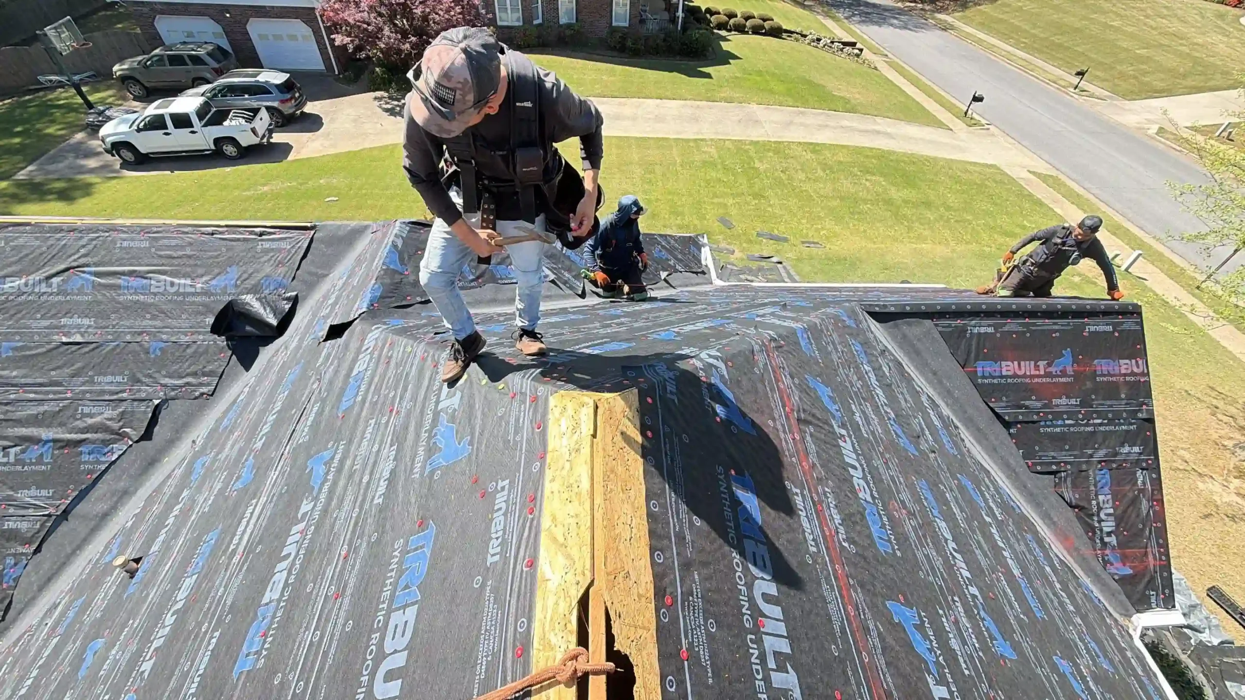 Two roofers working on a steep slope covered in black synthetic underlayment before shingle installation