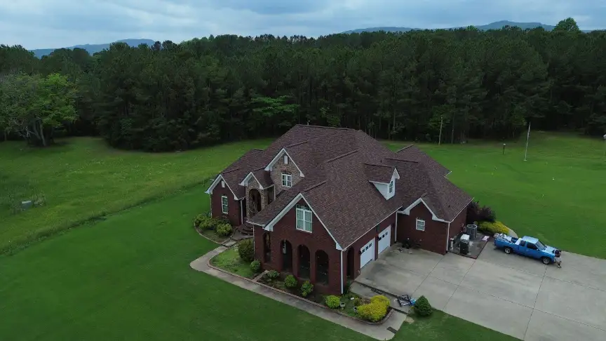 Large brick Scottsboro home with a finished roof set against a wooded foothill backdrop