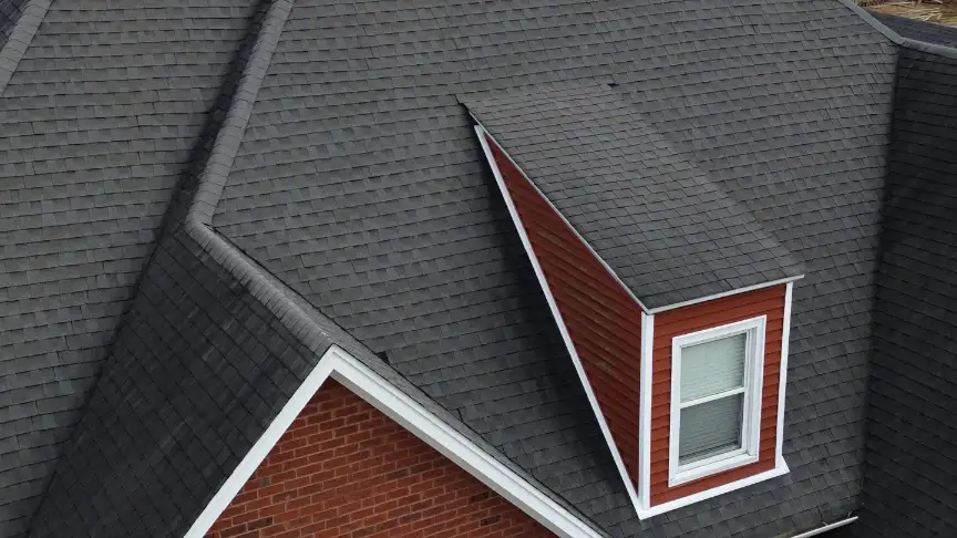 Close view of new dark gray shingles meeting a brick wall and a red-sided dormer