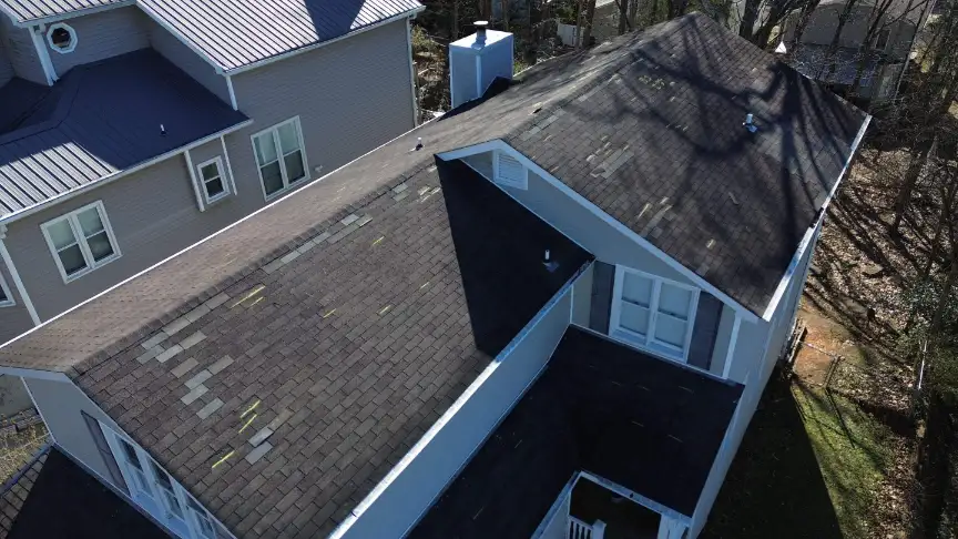 Aerial view of a weathered shingle roof where newer replacement shingles appear lighter than the sun aged originals