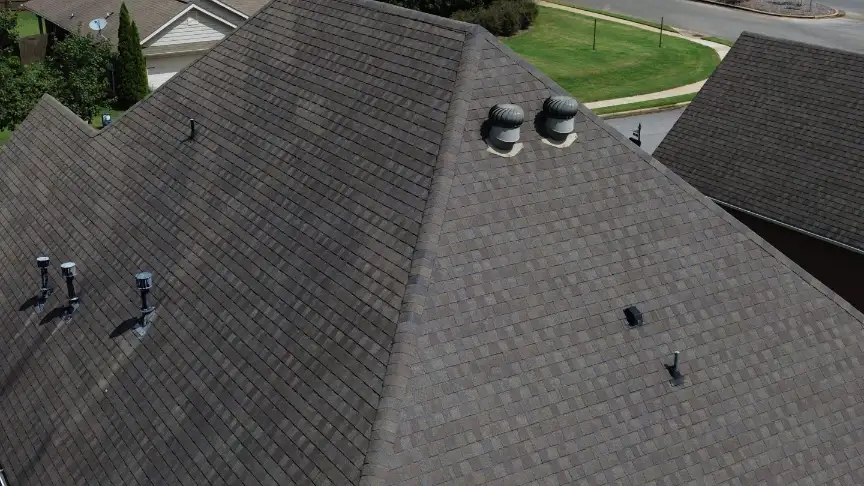 Finished brown shingle roof with roof vents and turbine vents among neighboring rooftops