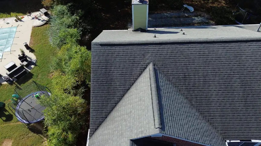 Finished shingle roof with a tall chimney above a backyard pool and trampoline