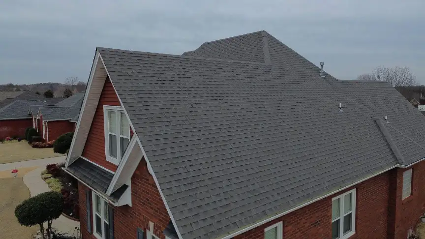 Completed steep gray roof on a large brick house under a cloudy sky