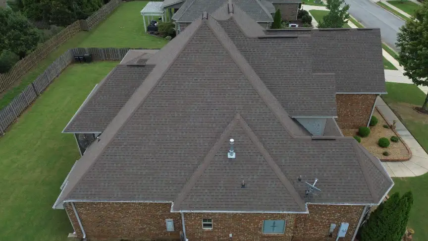 Complex brown shingle roof finished on a brick home with a fenced yard