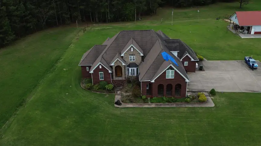 Brick home with a blue tarp over storm damage before the Moulton roof repair